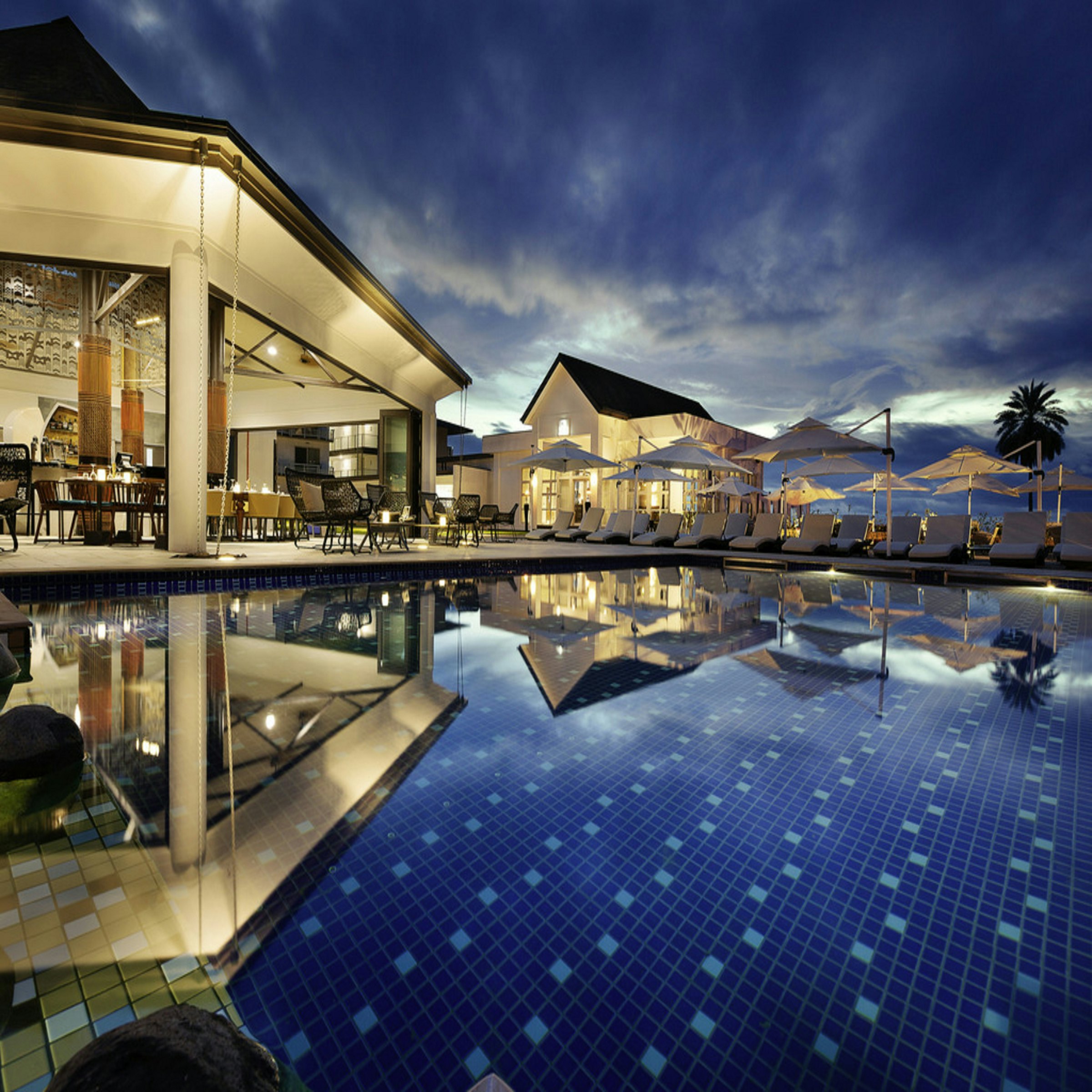 A hotel pool reflecting the lights of the pavilion at blue hour