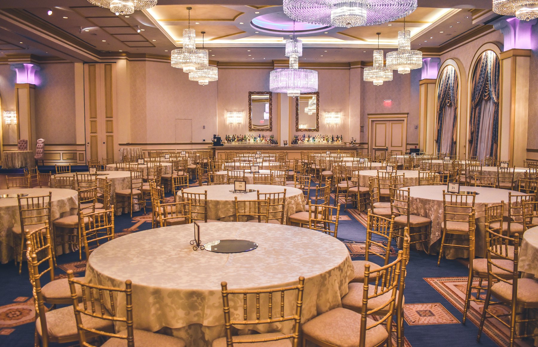 A gilded hotel ballroom set with round banquet tables and chandeliers