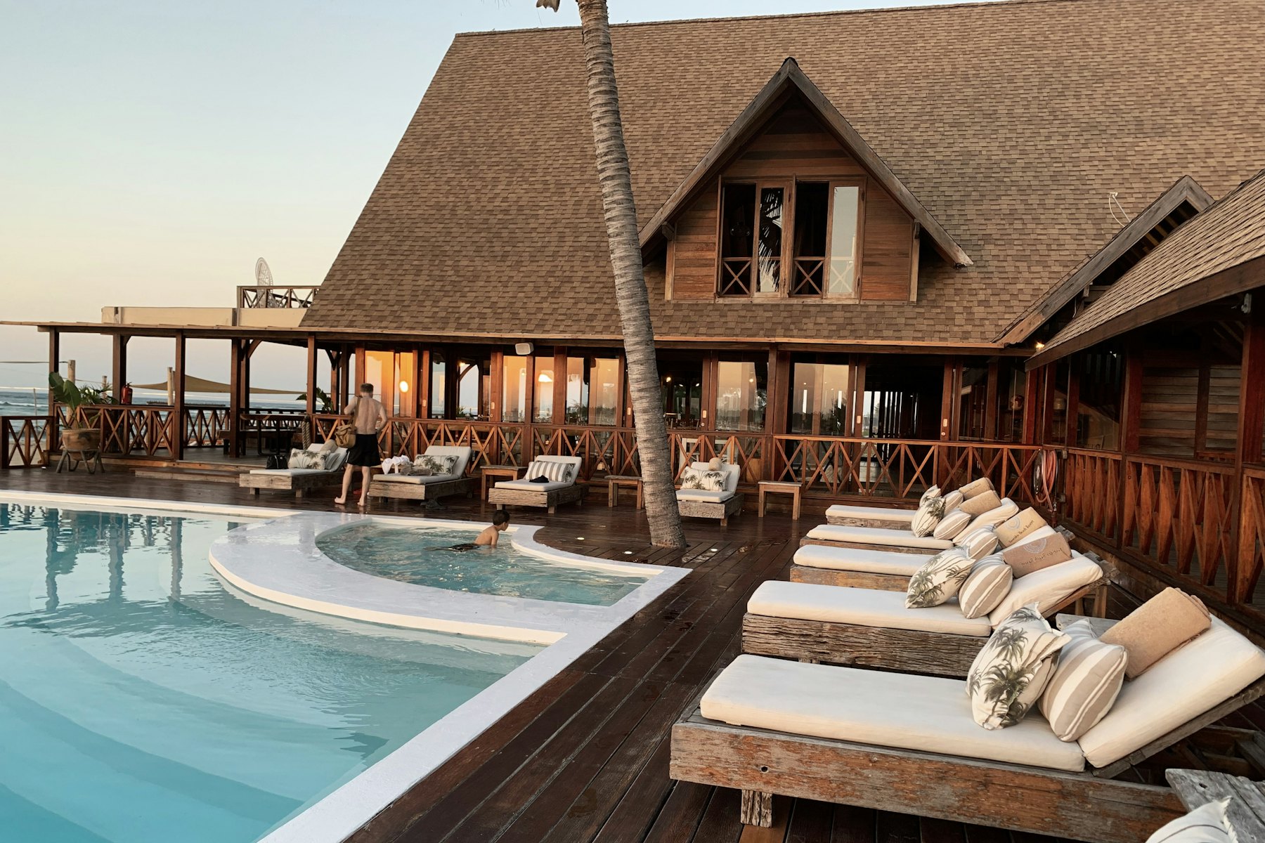 A timber resort pavilion and pool deck at sunset